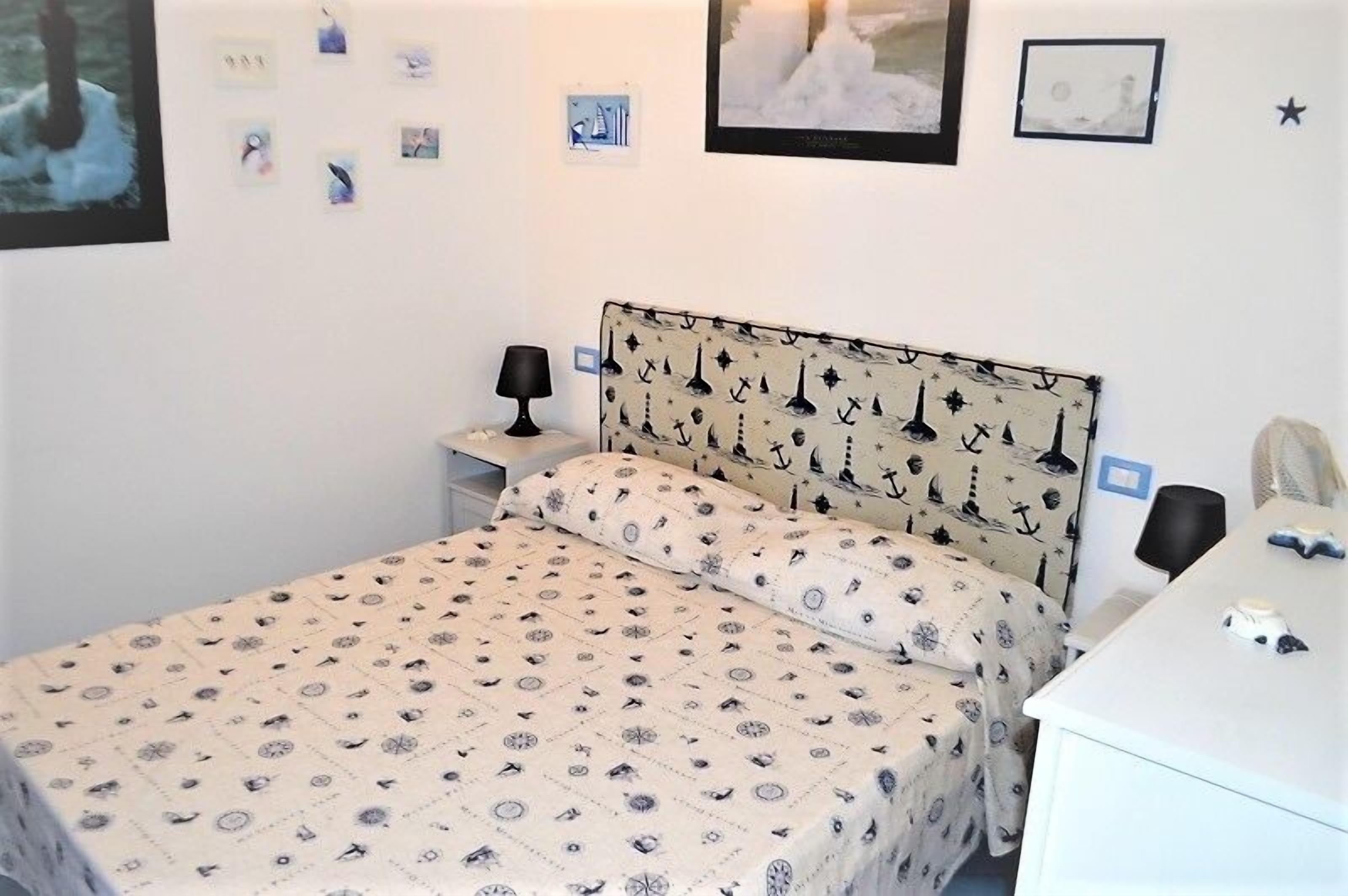 A bedroom with a bed, a bedside table, a lamp, and a small desk with a chair.