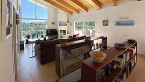Amplia sala de estar con una televisión grande, asientos cómodos, una estantería y vistas al exterior.