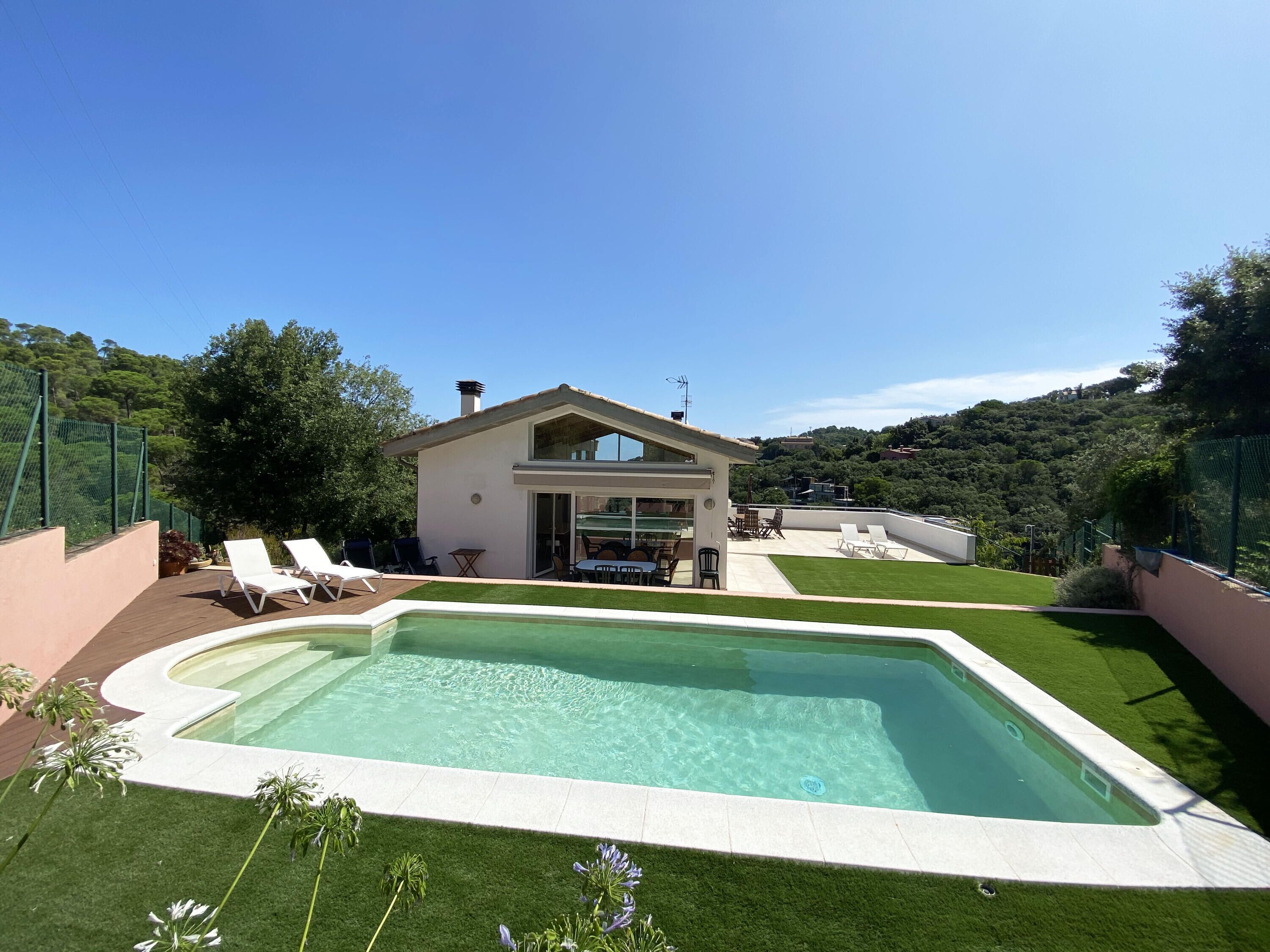 A modern house with a swimming pool, a patio with lounge chairs, and a view of a forested hillside.