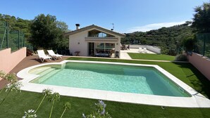 Una casa moderna con piscina, un patio con sillones de descanso y vistas a un paisaje boscoso.