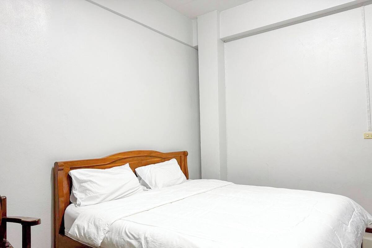 A single bed with a wooden headboard in a room with white walls and a plain ceiling.
