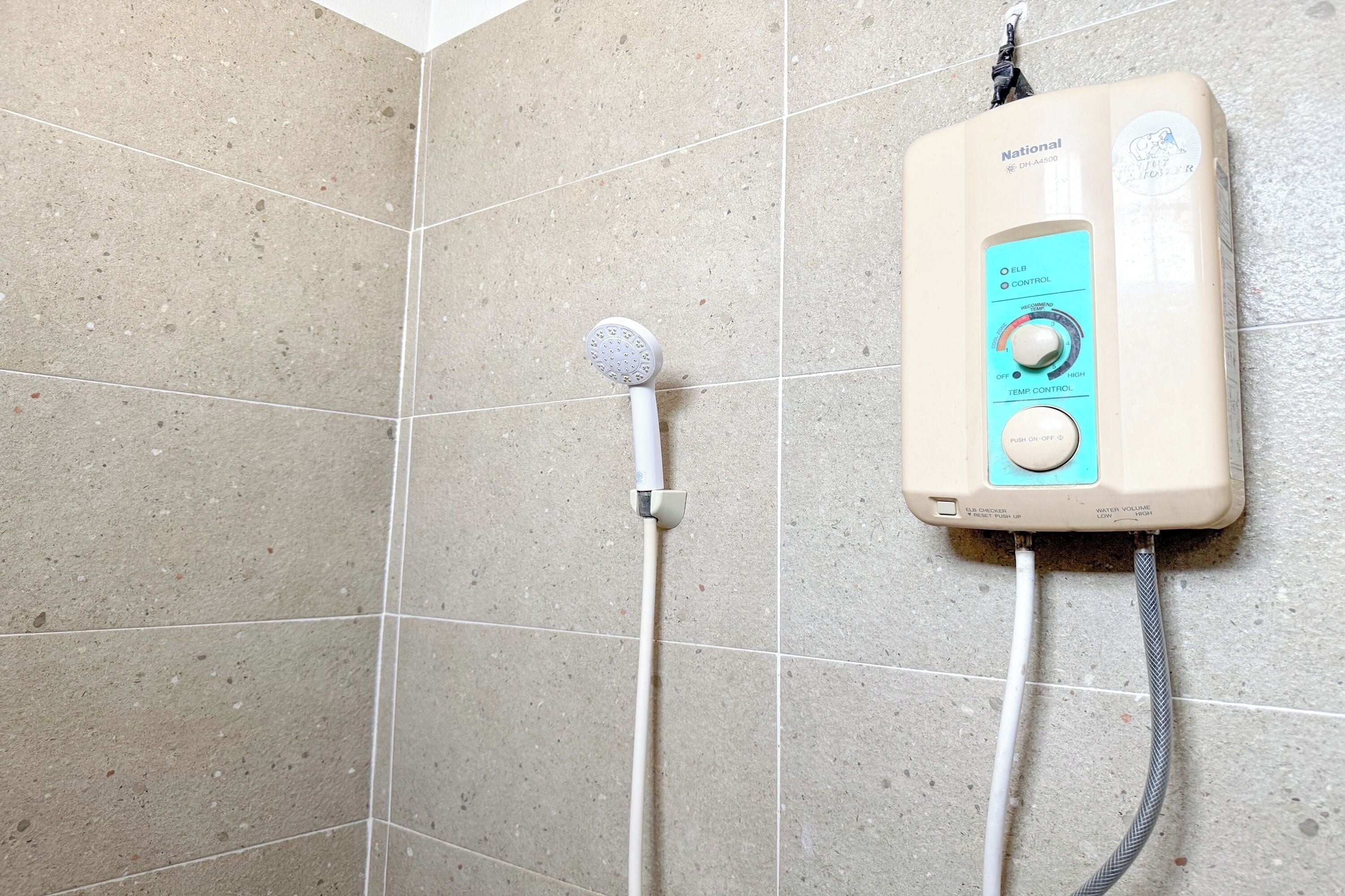 A shower area with a handheld showerhead and a wall-mounted control unit.