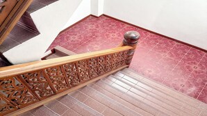 A wooden staircase with intricate carvings and a handrail, leading to a room with patterned red tiles. - Jitrawadee Hotel (Lampang)