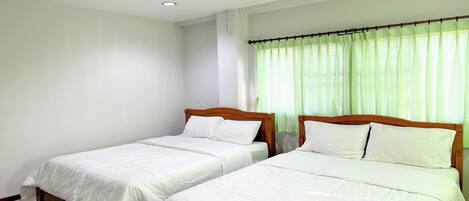 A room with two single beds, white bedding, wooden headboards, a window with green curtains, and a white wall.