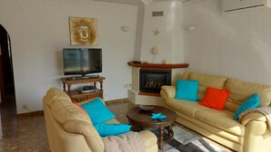 Una sala de estar con un sofá color beige, televisión, chimenea y conchas decorativas en la pared.