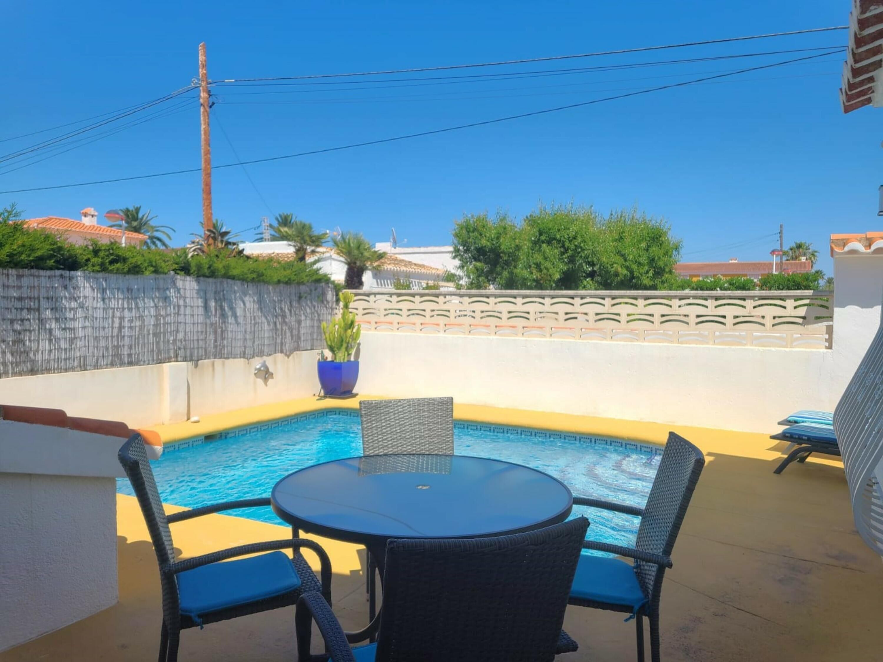 A pool area with a round table and four chairs, surrounded by a low wall and a decorative fence.