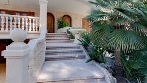 Un escalier en pierre menant à une porte en bois, entouré d’une végétation luxuriante et d’une balustrade blanche.
