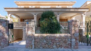 Une grande maison à deux étages, avec une entrée surmontée d’un mur en pierre, un balcon et un portail.