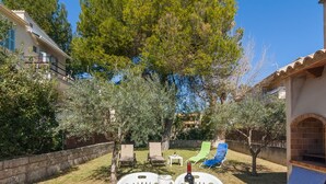 Un espace de restauration en plein air avec une table dressée pour quatre personnes, entouré d’oliviers et d’un mur en pierre.