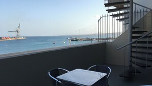 Een balkon met een tafel en stoelen, met uitzicht op een jachthaven vol boten en een schip in de verte.