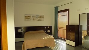 Een slaapkamer met een bed, nachtlampjes, een dressoir, een spiegel en een raam met jaloezieën.