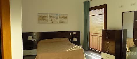 Un dormitorio con cama, lámparas de noche, cómoda, espejo y ventana con persianas.