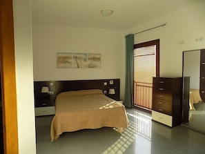 Un dormitorio con cama, lámparas de noche, cómoda, espejo y ventana con persianas.
