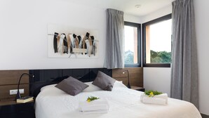 Une chambre d’hôtel moderne avec un grand lit, une table de chevet avec une lampe, une œuvre d’art murale et une fenêtre avec des rideaux.