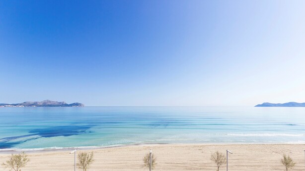 Une plage à l’eau d’un bleu limpide, bordée d’un rivage sablonneux, avec des montagnes qui se dessinent à l’horizon.