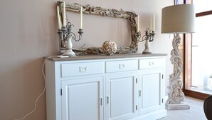 Un mueble blanco con tres cajones, un espejo decorativo con marco rústico y una lámpara blanca encima.