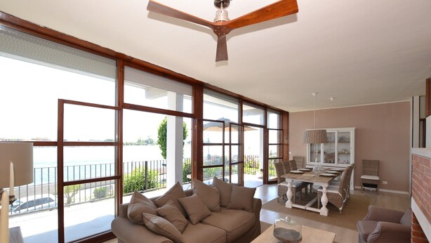 Amplia sala de estar con un ventanal grande, ventilador de techo y comedor con mesa dispuesta para cuatro.