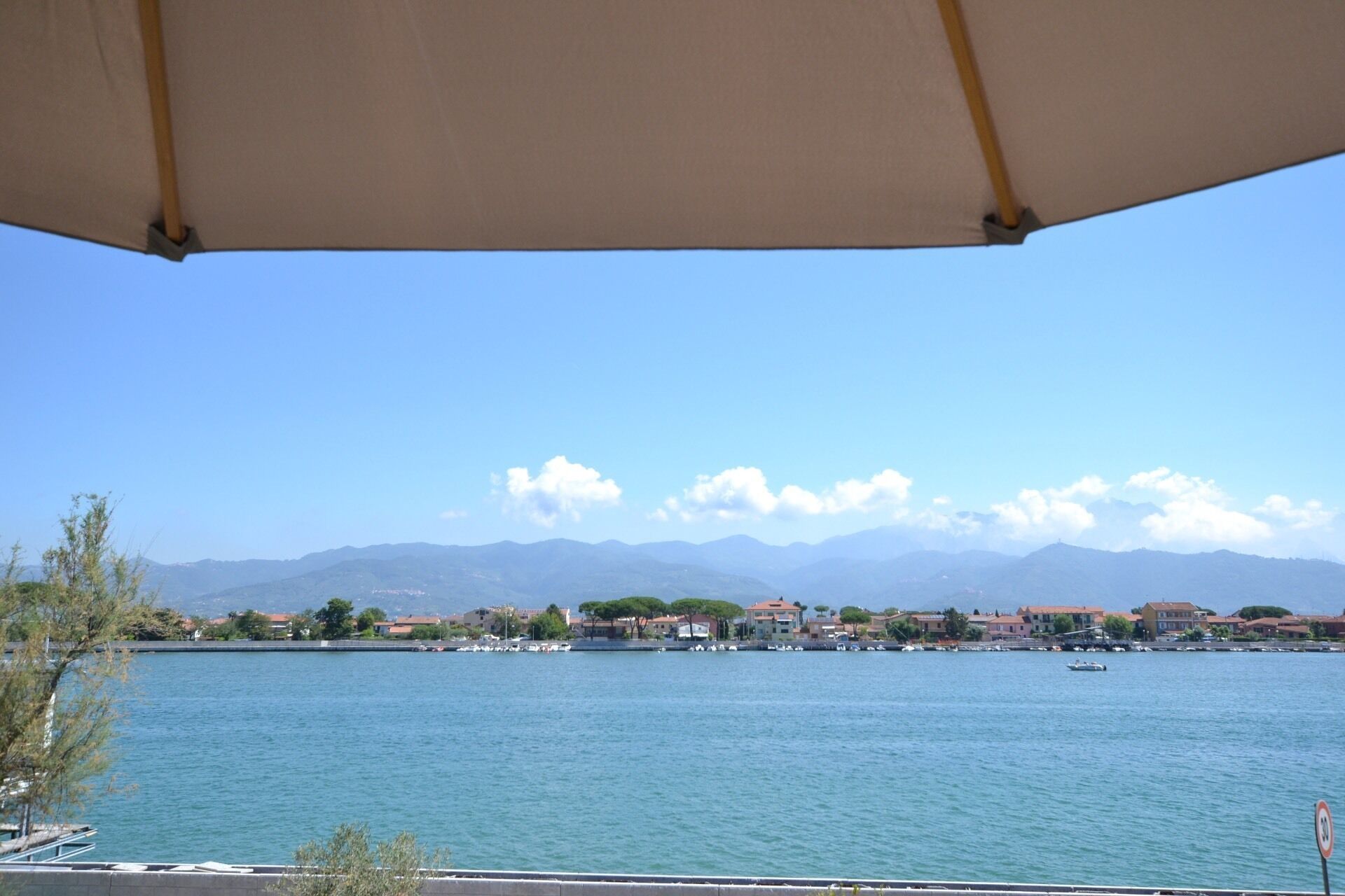 A waterfront view with a clear sky, mountains in the background, and a row of buildings along the shore.