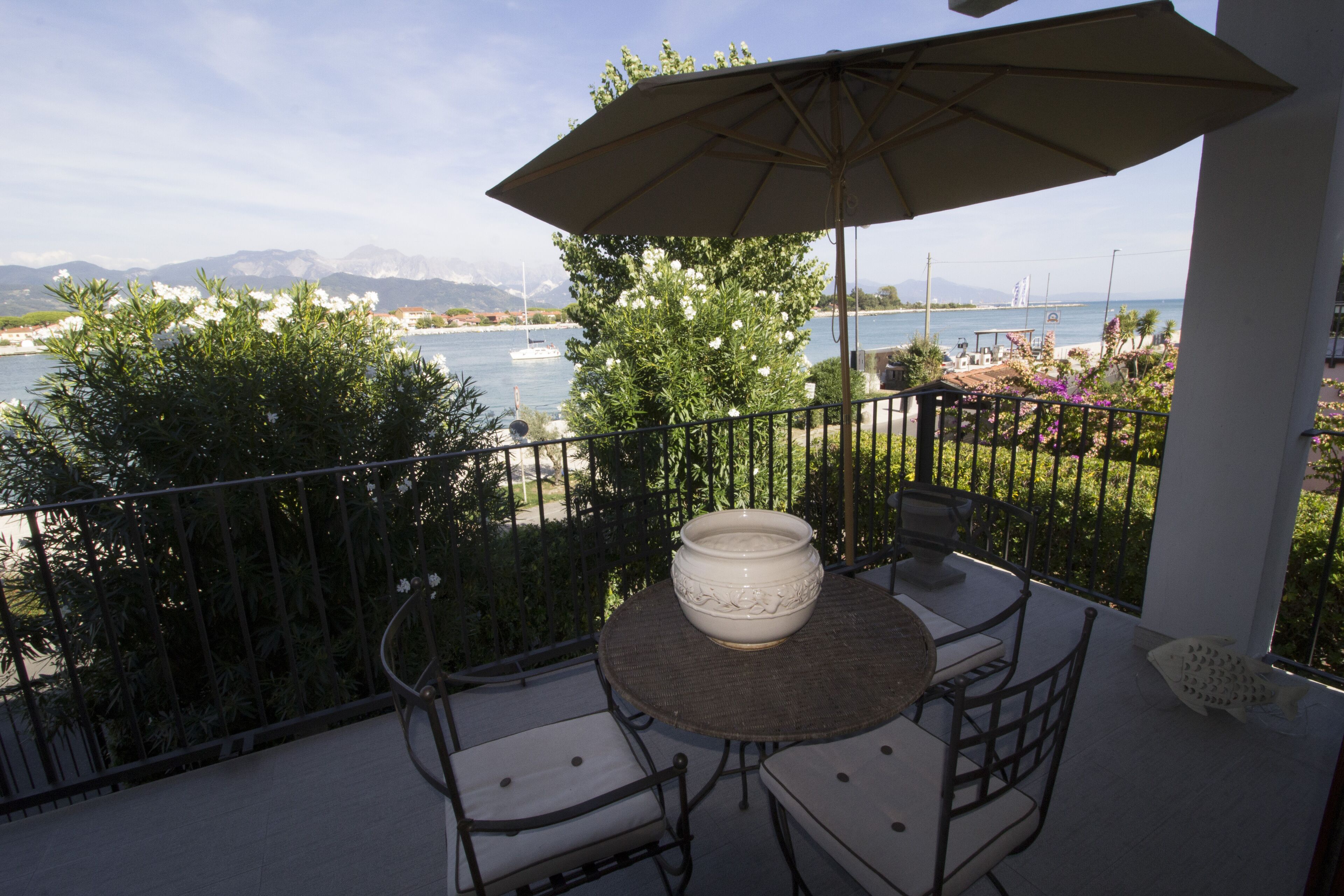 Een balkon met een tafel en stoelen, een grote parasol en uitzicht op zee en bergen.