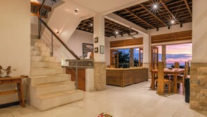 A spacious interior with a staircase leading to a balcony, a dining area with wooden furniture, and a view of the sunset. - Luxury villa close to Lovina with pool and staff and spectacular views! (Temukus/Lovina)