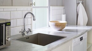 A kitchen with white cabinets, a stainless steel sink, a wooden bowl on the counter, and a window above the sink.