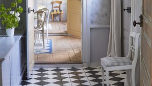A room with a checkered floor, a white chair, a wooden door, and a potted plant.