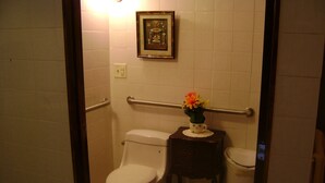 Une salle de bain avec deux toilettes, une petite table sur laquelle est posé un vase de fleurs et un tableau encadré au mur.