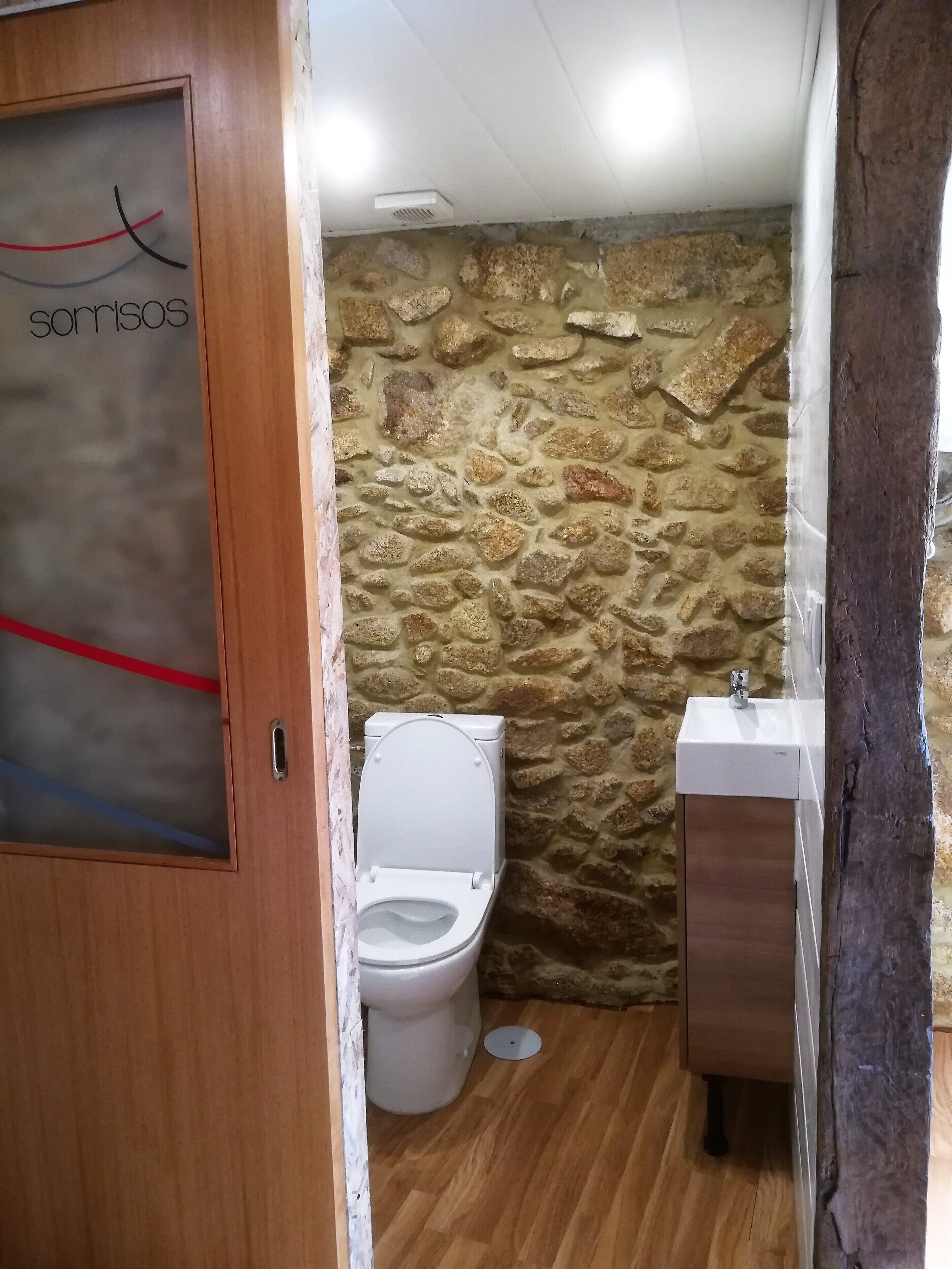 A bathroom with a stone wall, wooden floor, a toilet, and a sink.