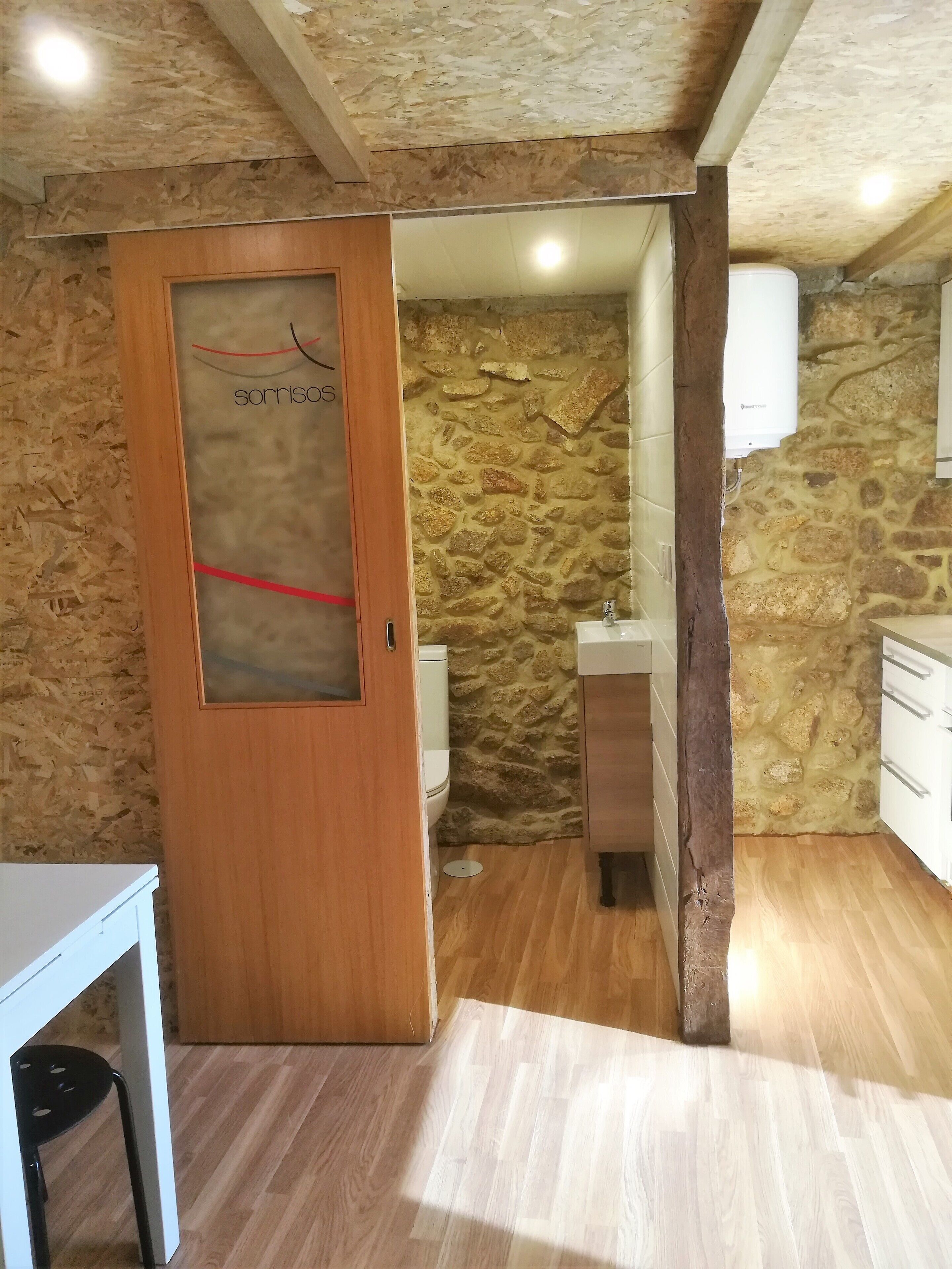 Een kleine badkamer met een stenen muur, een houten deur en een wit wastafelmeubel.