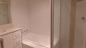 Ein modernes Badezimmer mit einer gläsernen Duschkabine, einer weißen Badewanne und einem Waschtisch mit Schubladen.
