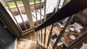 A modern interior with a wooden staircase, a dining area with a table set for four, and a view of a patio with outdoor furniture. - 5 star luxury apartment m. daily cleaning, fireplace u. great water view (Loddin)