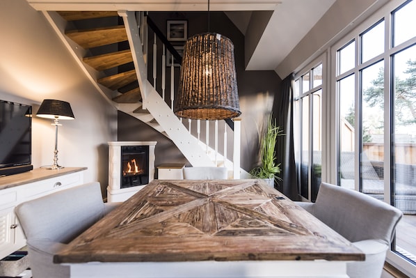 A modern living room with a large wooden coffee table, a fireplace, a staircase, and large windows.