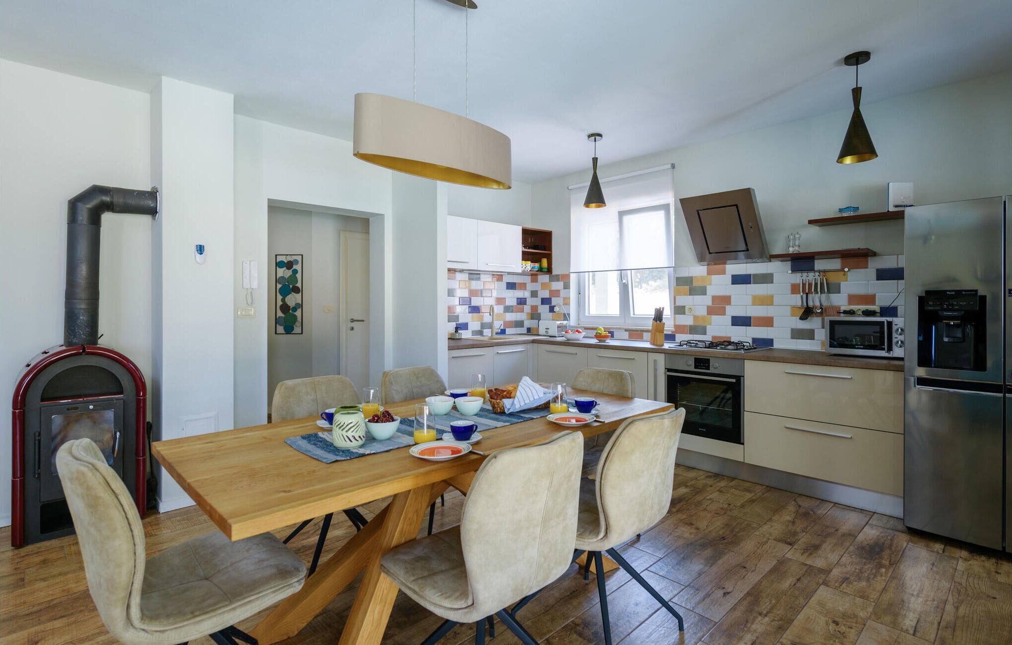 Una cucina moderna con zona pranzo, che include un tavolo in legno, sedie, forno a incasso, microonde e frigorifero.