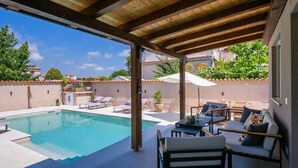 A poolside area with a pool, lounge chairs, a table with chairs, and a covered patio. - Luxurious home in Medulin (Medulin)