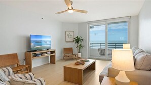 Ein modernes Wohnzimmer mit Fernseher, Couch, Holztisch und einem Balkon mit Meerblick.