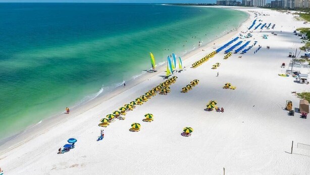 Ein Strand mit Reihen von Sonnenschirmen und Liegestühlen, einem klaren blauen Himmel und ruhiger See.