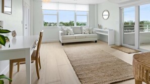 Ein geräumiges Wohnzimmer mit einem weißen Sofa, einem Esstisch mit Stühlen, einem Deckenventilator, großen Fenstern und Blick ins Freie.