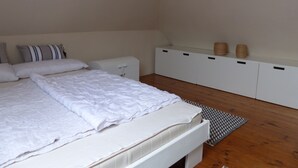 A bedroom with a bed, pillows, a bedside table, a storage unit, and a herringbone-patterned rug. - *'CLOSE TO THE BEACH*'ALLERGY FRIENDLY**MAISONETTE APARTMENT**UP TO 4 PERSONS**BALCONY*** (Friedrichskoog-Spitze)
