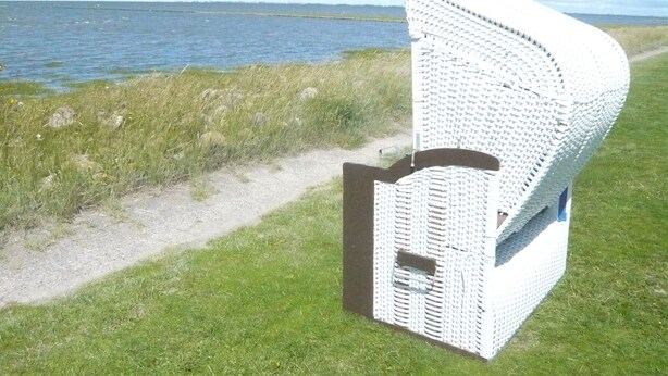 A white wicker chair with a curved backrest and a metal frame, positioned on a grassy area near a body of water. - *'CLOSE TO THE BEACH*'ALLERGY FRIENDLY**MAISONETTE APARTMENT**UP TO 4 PERSONS**BALCONY*** (Friedrichskoog-Spitze)