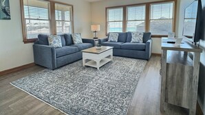 A living room with two sofas, a coffee table, a TV, and a ceiling fan. - Pelican Place Cottage- Short walk to beach- Community Pool & Spa (Buxton)