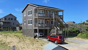 A two-story building with a balcony on the second floor, a covered front porch, and a garage. - Pelican Place Cottage- Short walk to beach- Community Pool & Spa (Buxton)