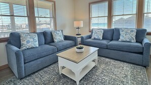 A living room with two blue sofas, a white coffee table, and a patterned rug. - Pelican Place Cottage- Short walk to beach- Community Pool & Spa (Buxton)