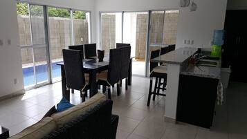 A modern kitchen with a bar area, a dining area with wicker chairs, and a view of a swimming pool through large glass doors.
