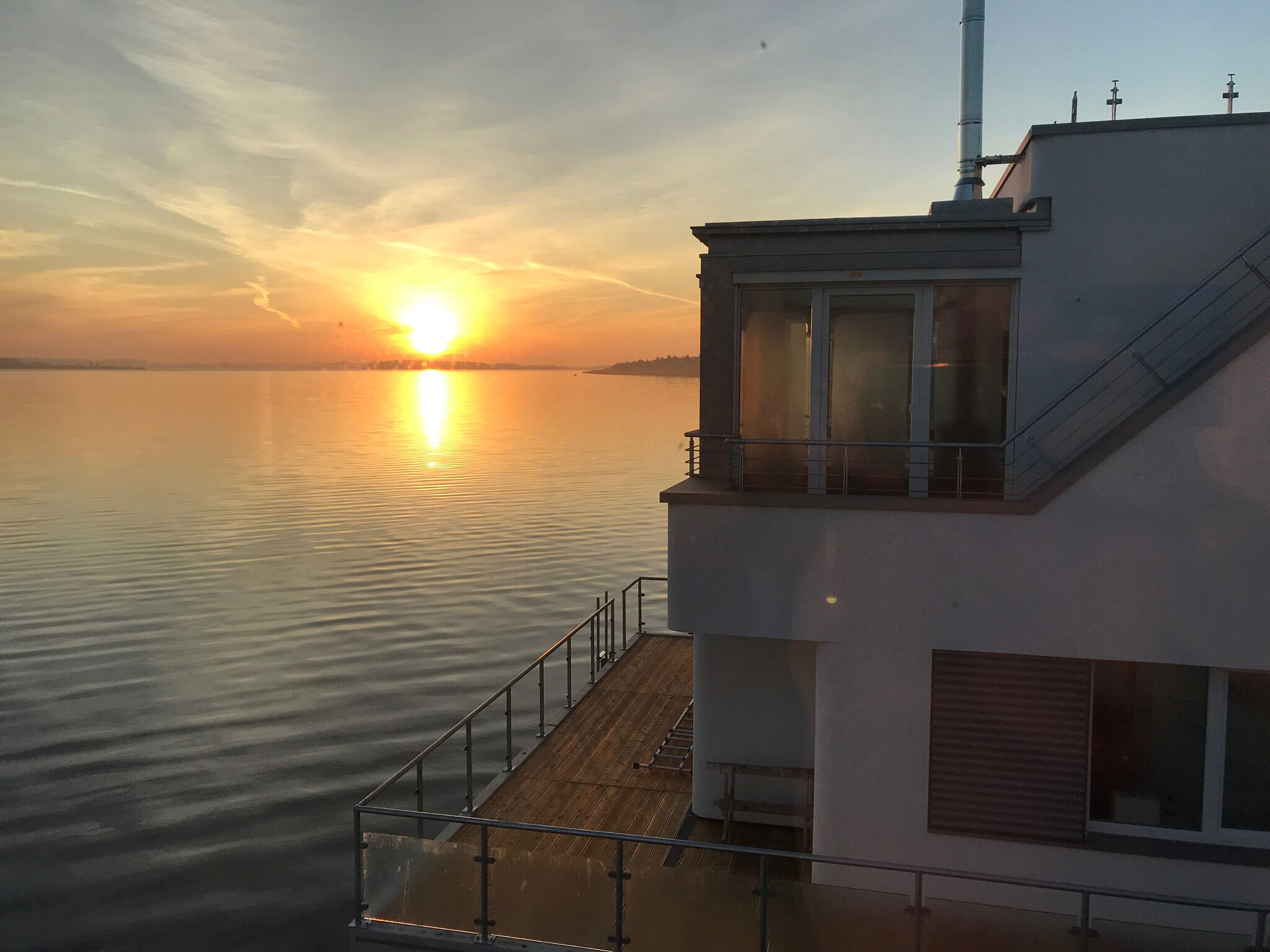 A building with a balcony overlooking calm water during sunset.