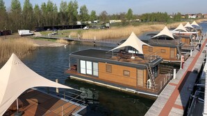Alojamiento a orillas del río con terraza de madera, zona de estar cubierta y vistas al río y árboles.