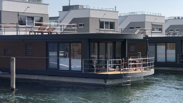 Una casa flotante moderna con terraza, ventanas amplias y vista al agua.
