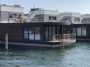 Et moderne flydende hus med terrasse, store vinduer og udsigt til vandet.