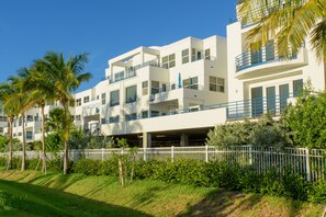 Um hotel moderno de vários andares com varandas, área de estacionamento coberta e vegetação exuberante.