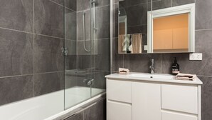 Un baño moderno con ducha envuelta en vidrio, una bañera blanca y un tocador con espejo.