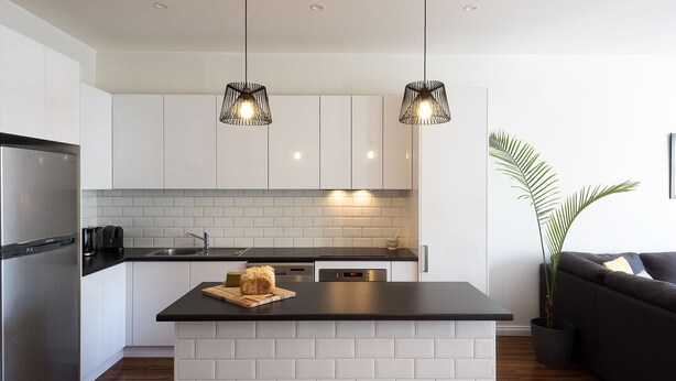 Una cocina moderna con armarios blancos, encimera negra y dos lámparas colgantes.